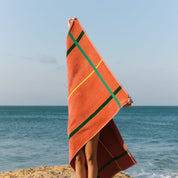 Person holding an cognac beach towel with green and yellow stripes on a beach