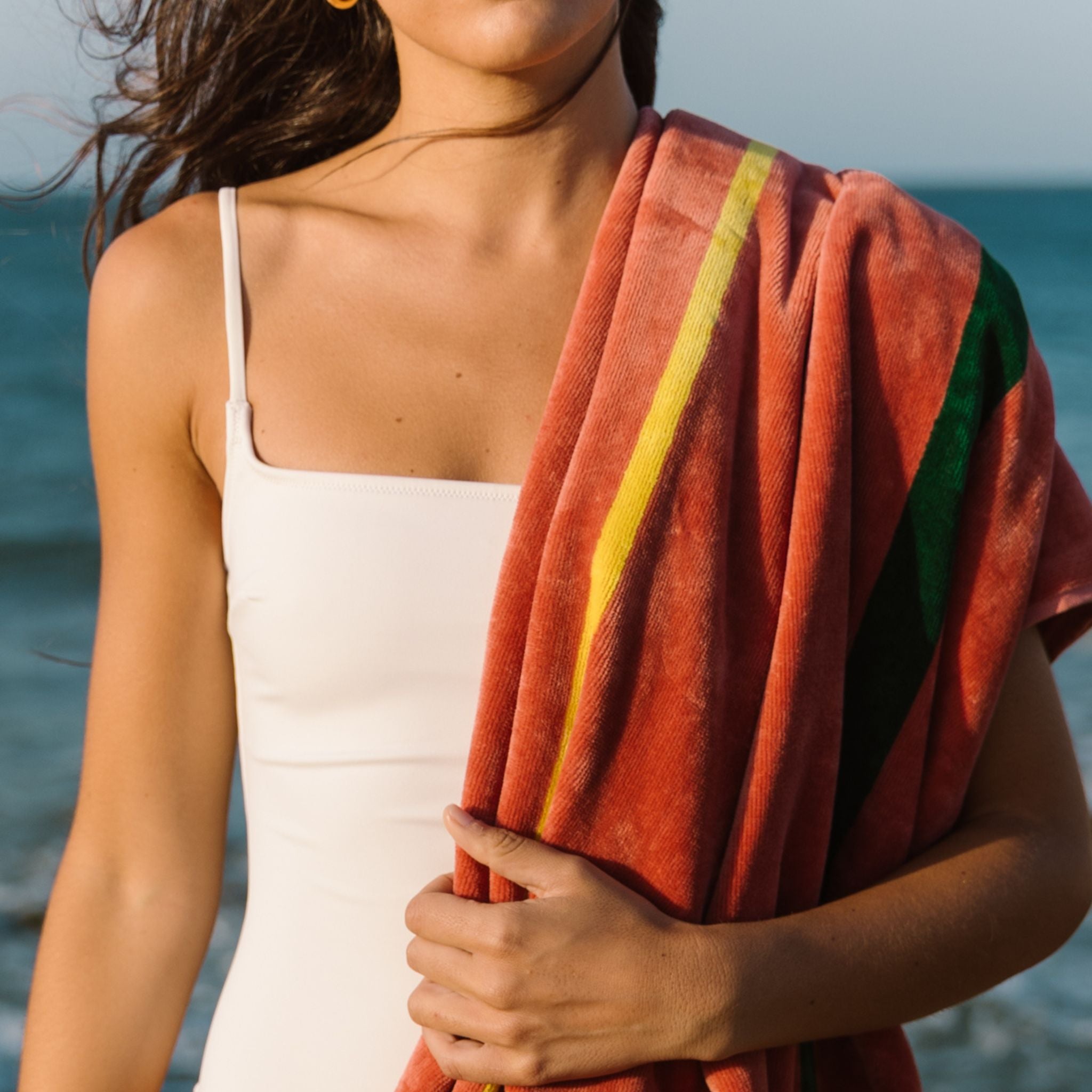 Woman holding a colorful towel by the ocean