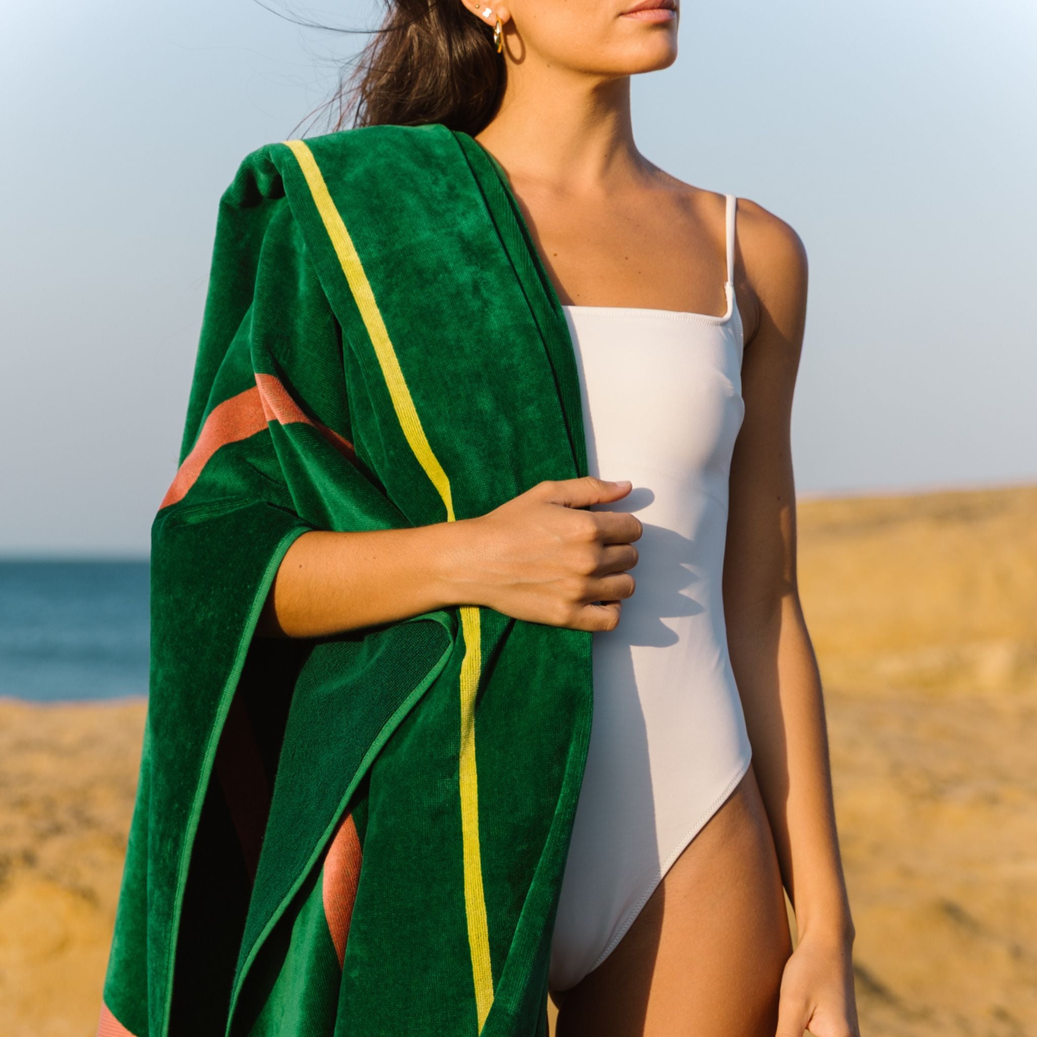 Woman in a white swimsuit holding a green beach towel on a beach