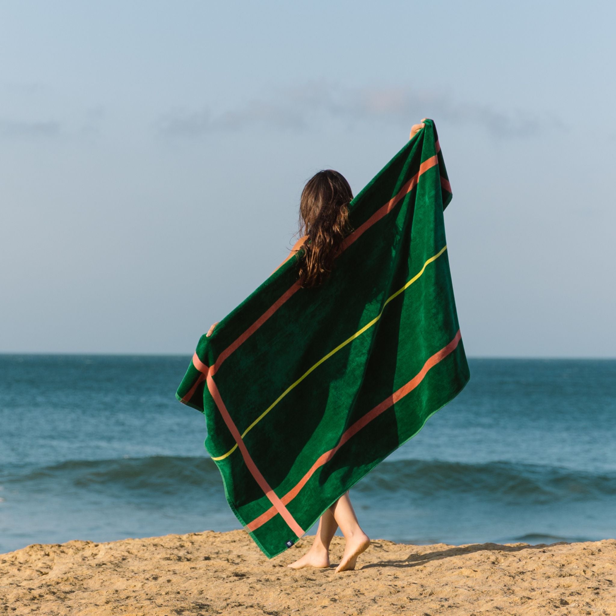 Person wrapped in a green beach towel on a beach with ocean view