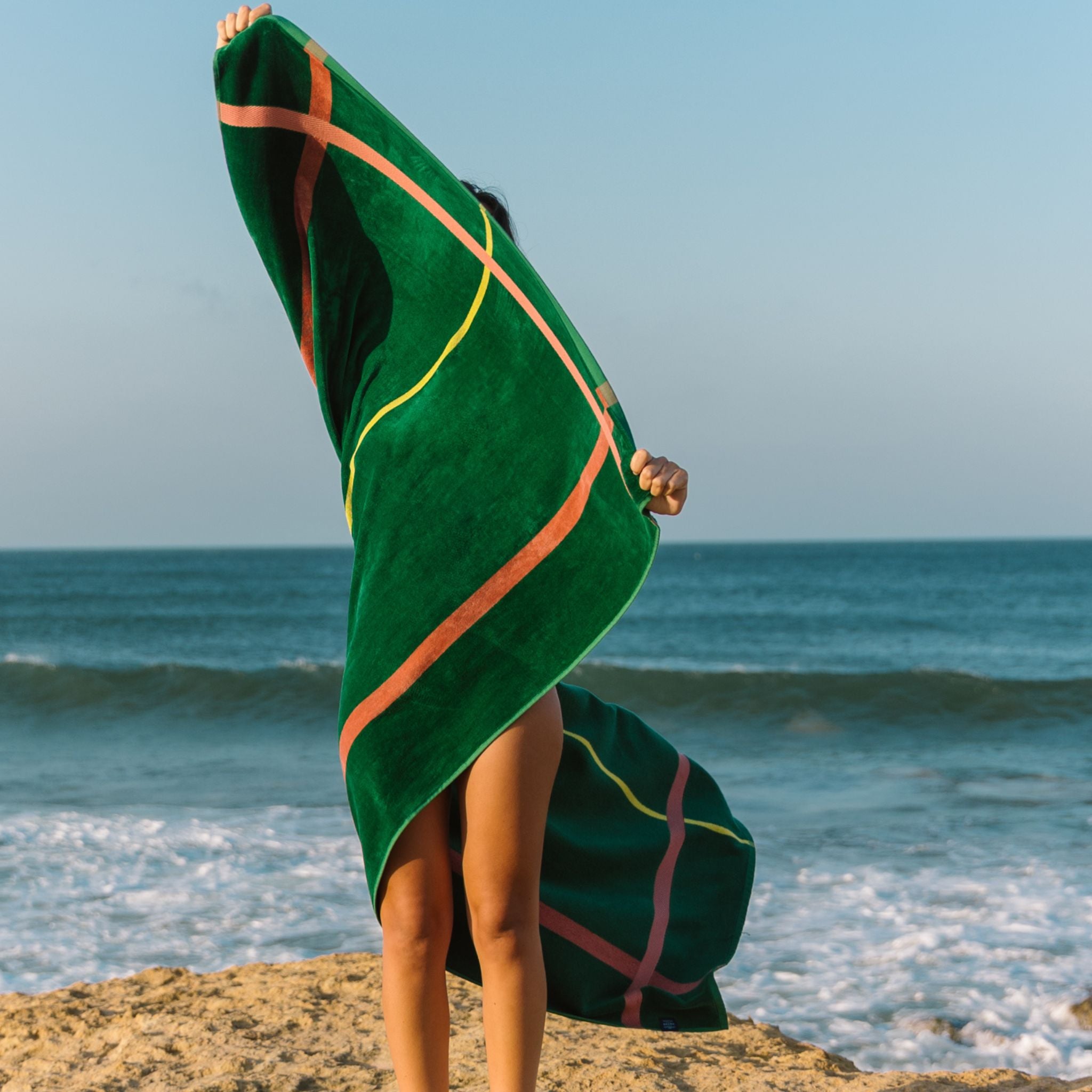 Person holding a green beach towel with yellow and cognac lines on a beach