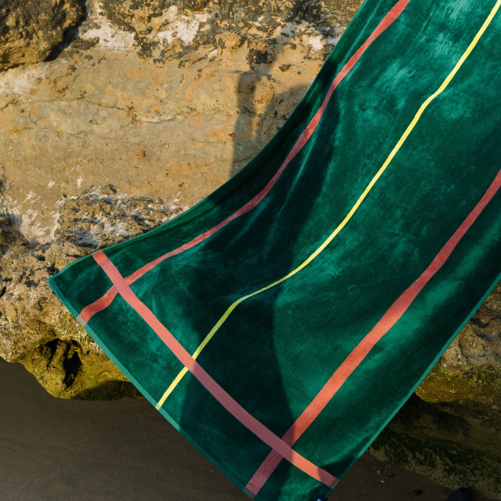 Green beach towel with cognac and yellow lines draped over a stone surface
