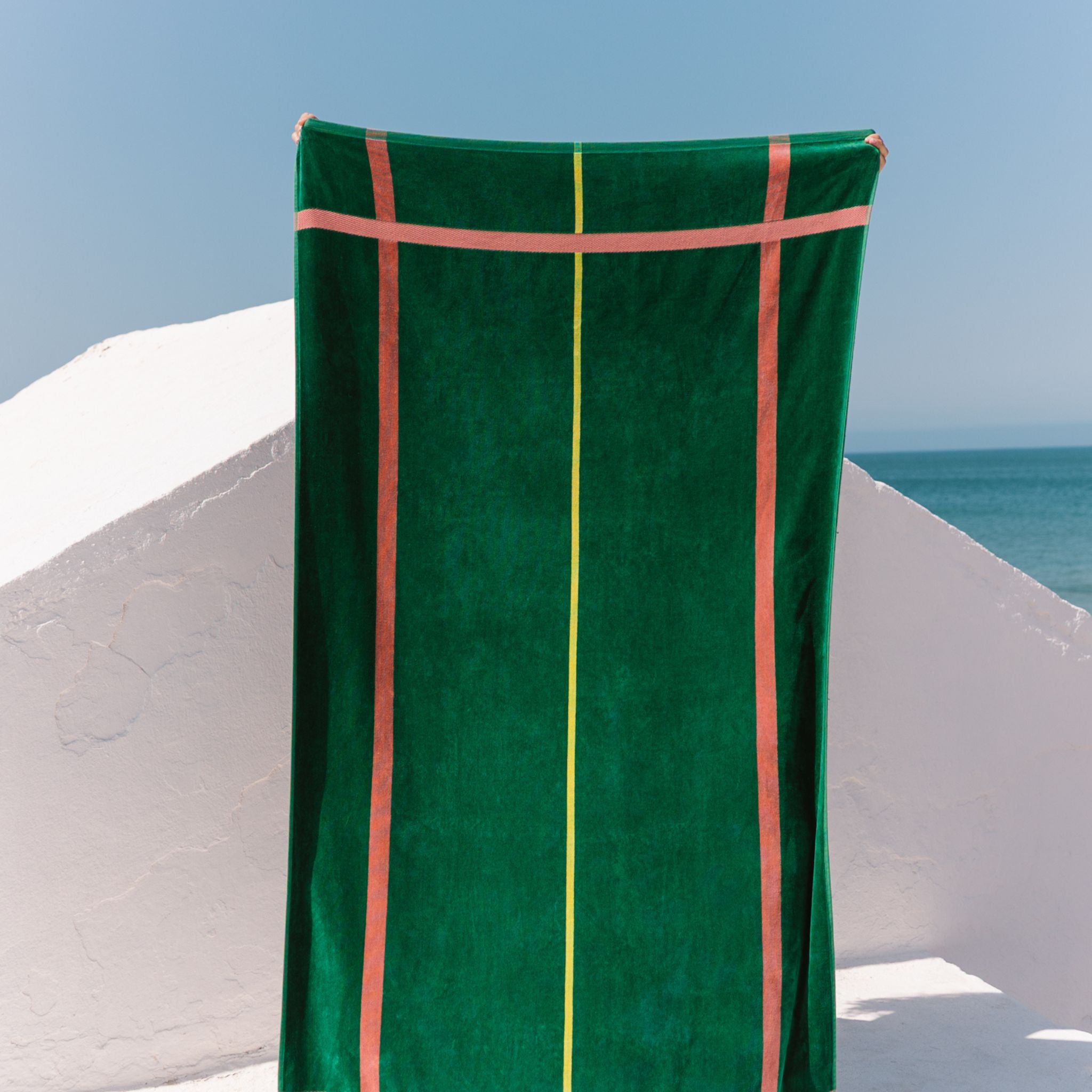 Green towel with cognac stripes draped over a white wall with ocean view