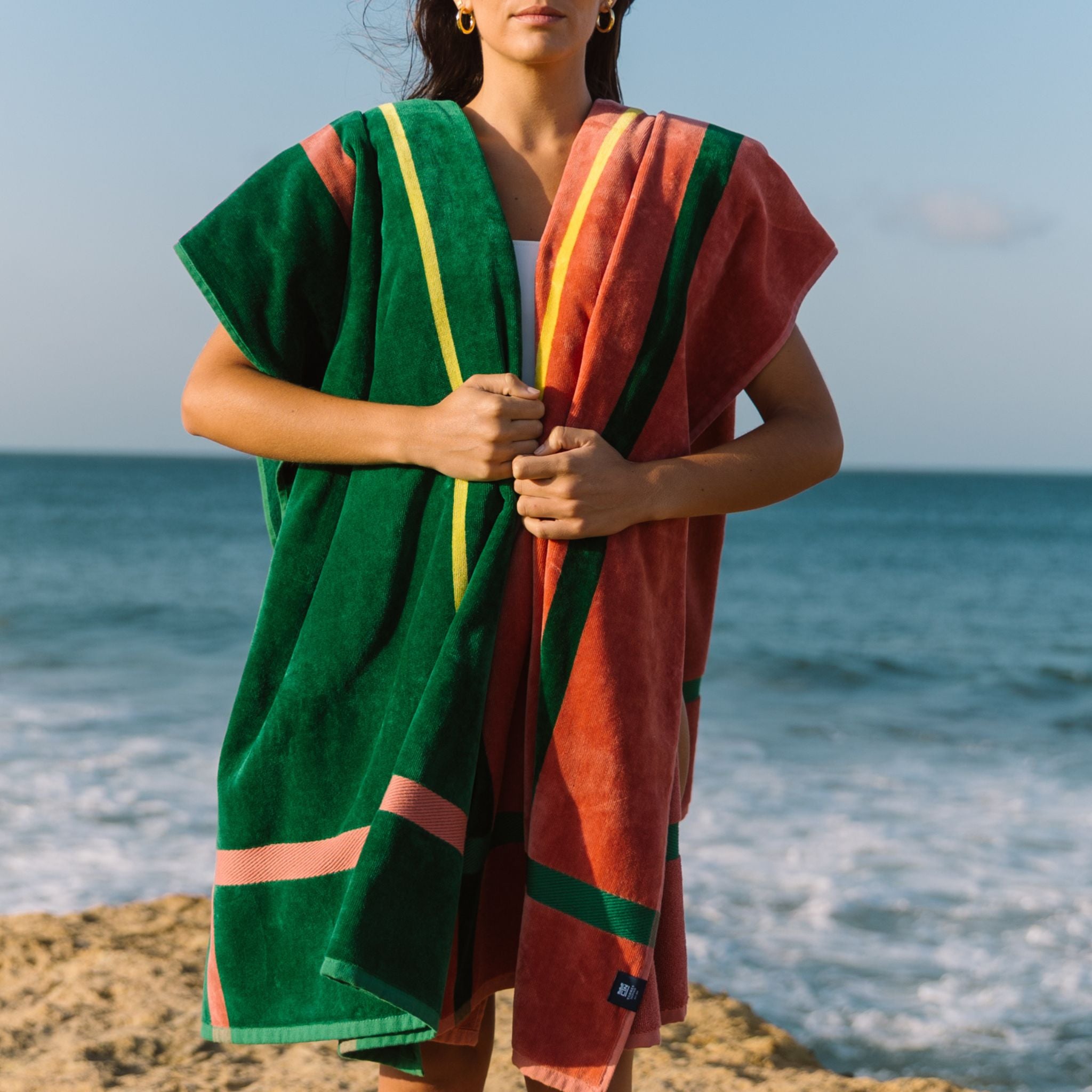 Person holding a green and cognac beach towels with ocean in the background
