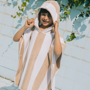 Child wearing a beige and white striped poncho with a hood, standing against a light blue tiled wall.