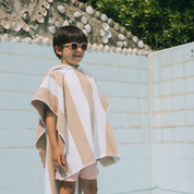 Child wearing a striped poncho and sunglasses by a poolside.