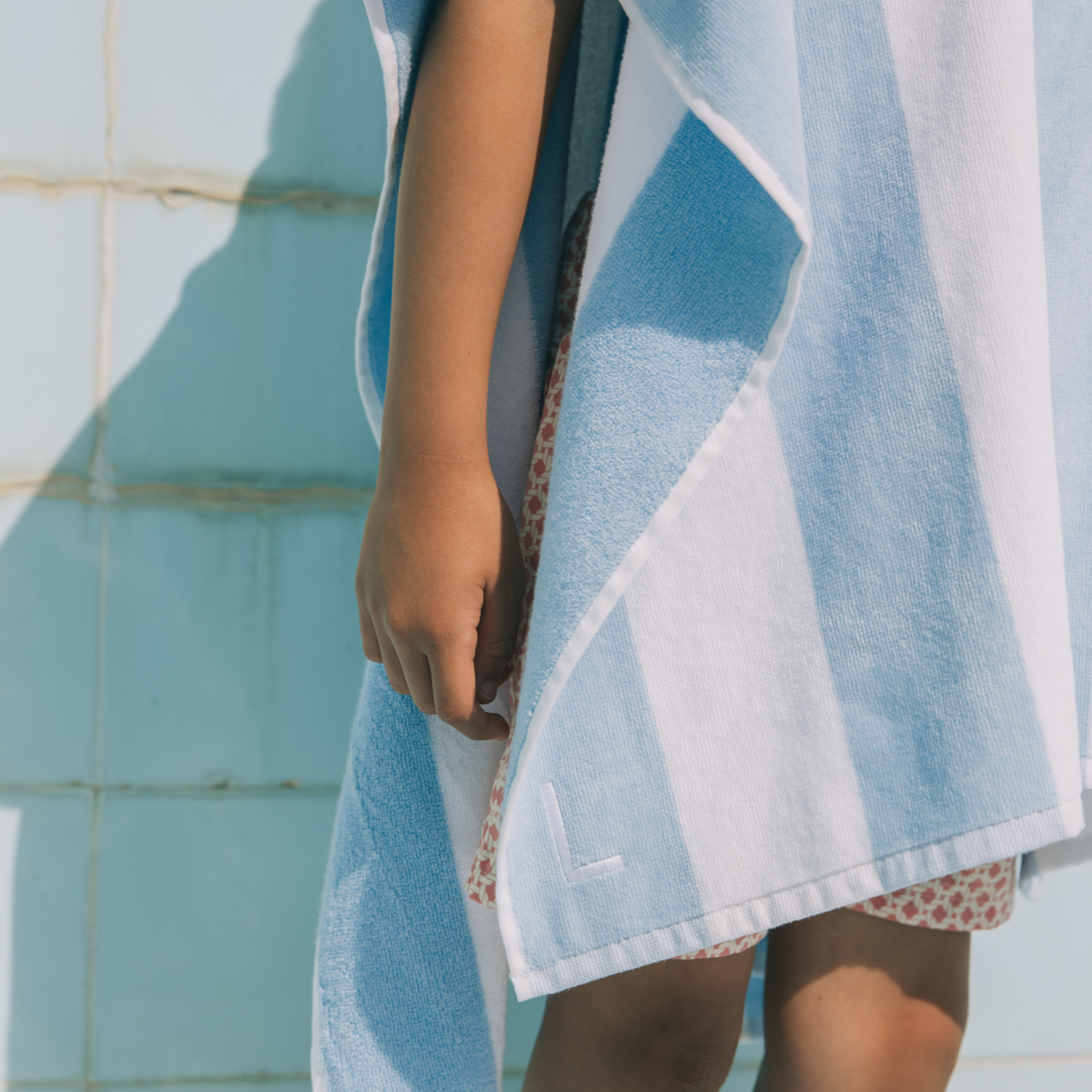 Kid wrapped in a blue and white poncho by a pool.