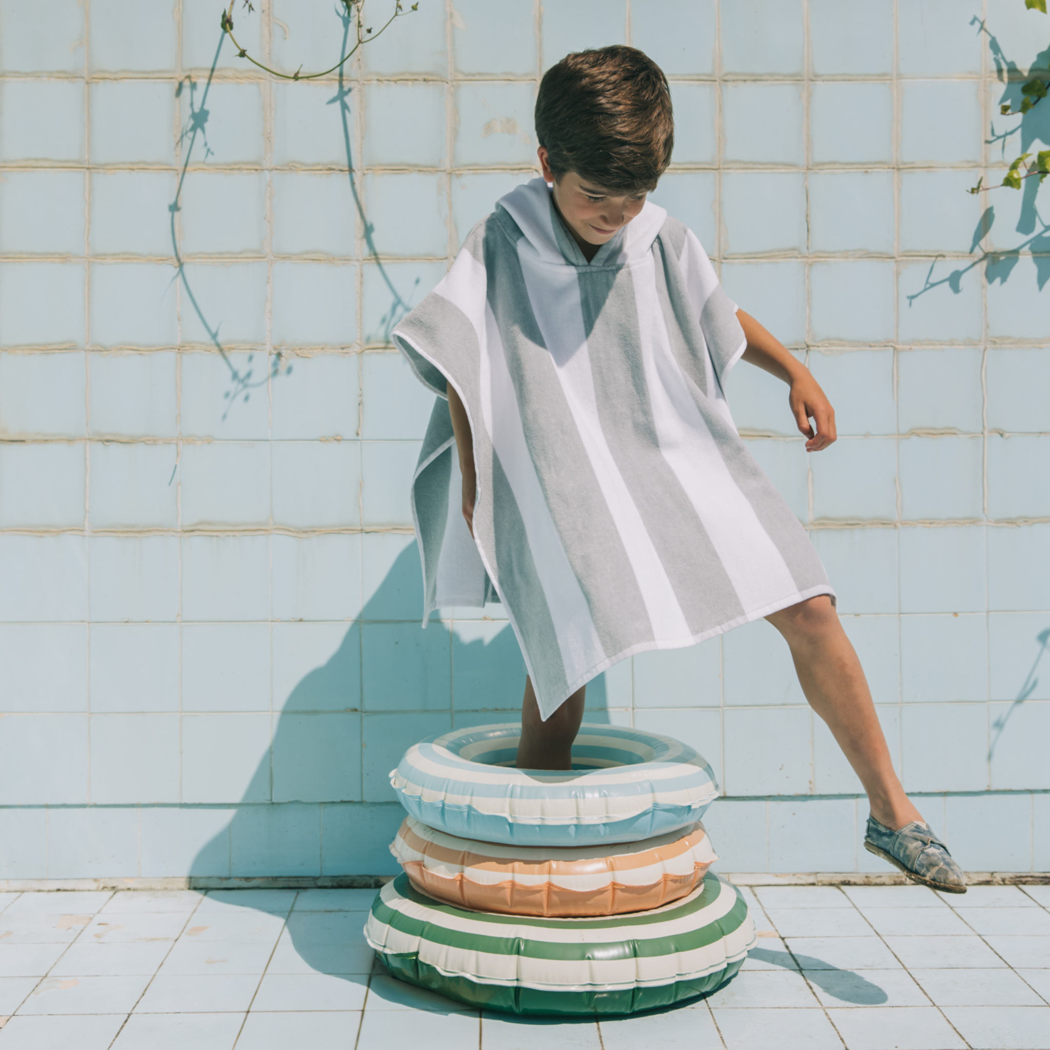 Kid standing on a stack of colorful inflatable rings against a tiled wall.