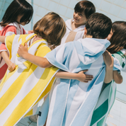 Children wrapped in colorful striped ponchos hugging each other outdoors.