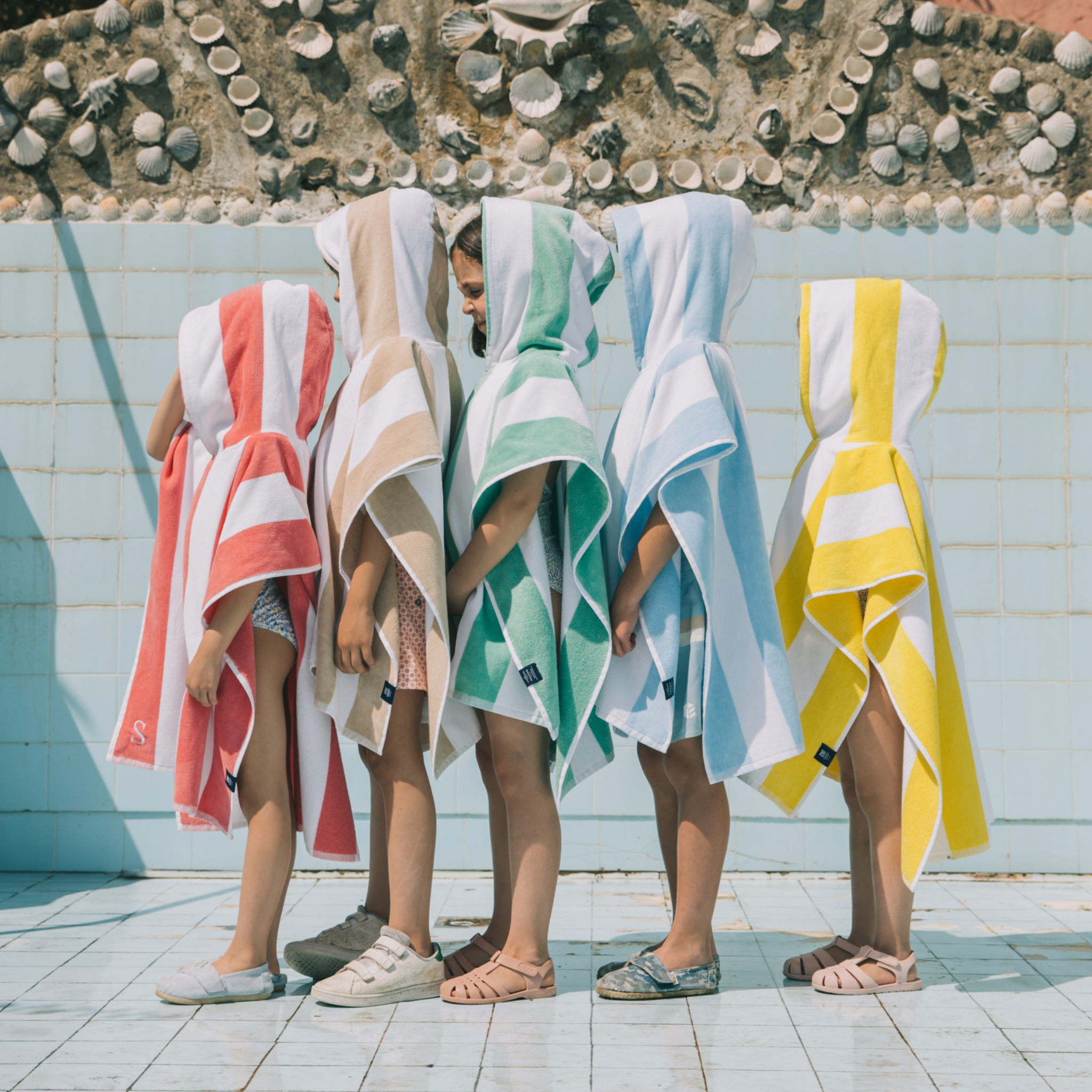 Children wearing colorful hooded ponchos by a poolside.