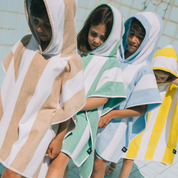 Four children wearing colorful hooded ponchos in a pool setting.