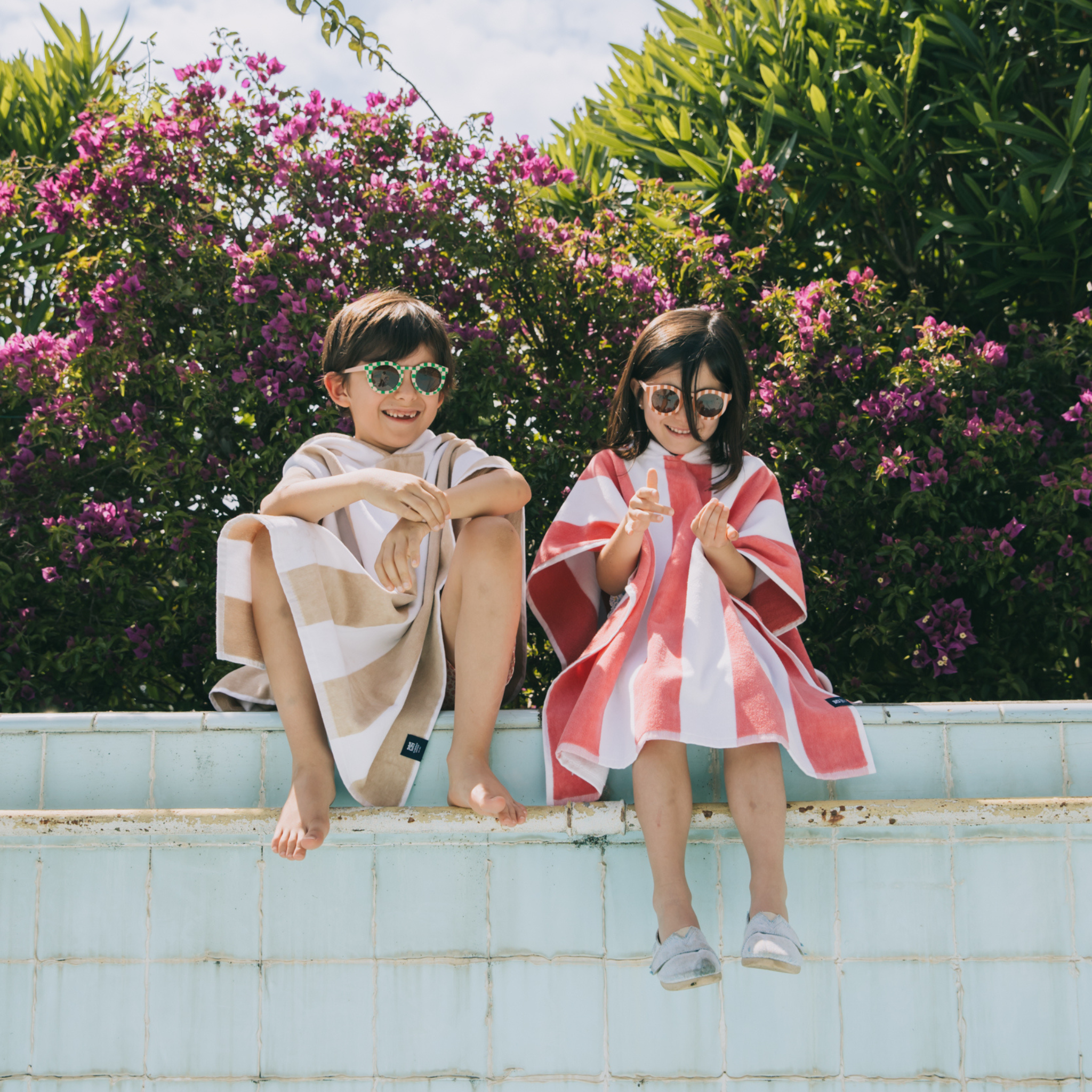 Two children sitting on a ledge with floral and greenery background