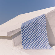 Blue checkered beach towel on a white wall with a clear blue sky.