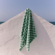 Green checkered beach towel draped over a white wall with a blue sky background