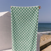 Green checkered towel held up against a beach backdrop