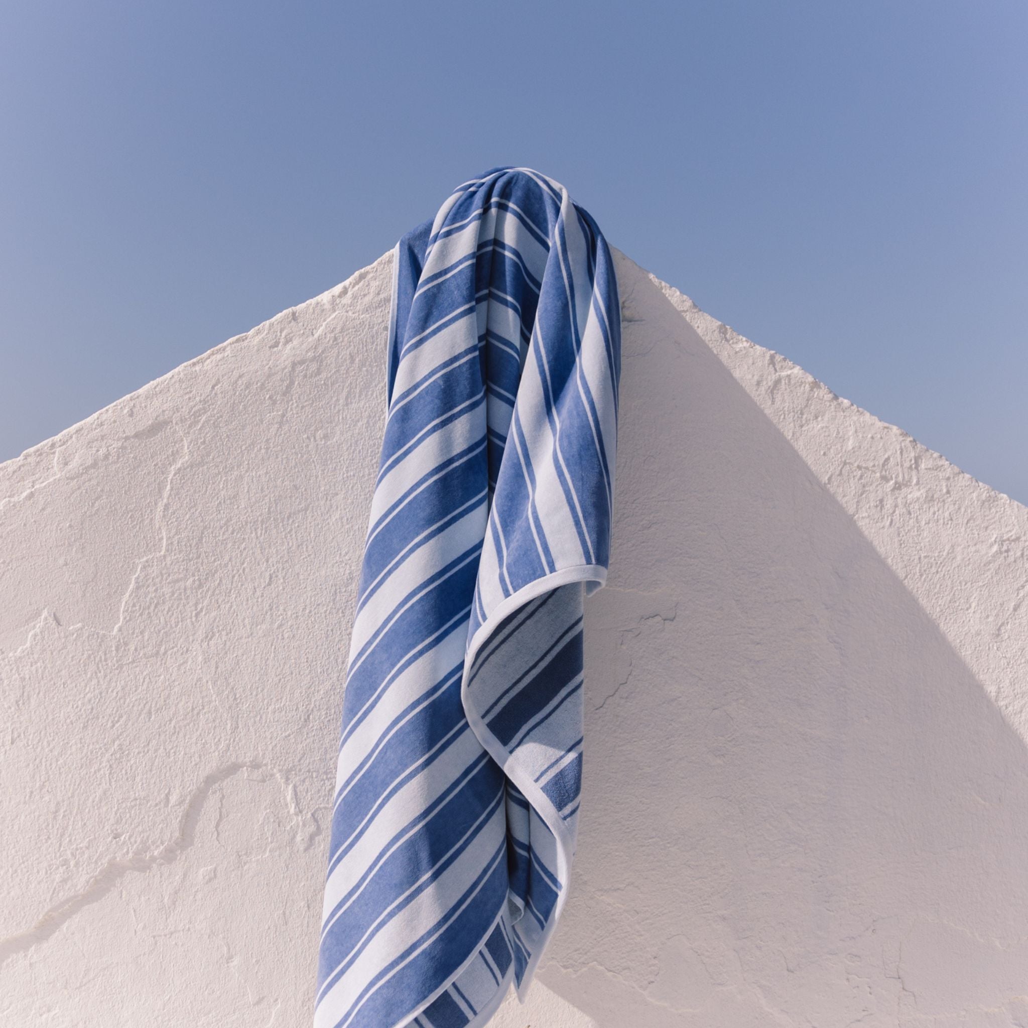 Blue striped beach towel hanging on a white wall with a clear blue sky.