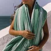 Person wearing a green striped beach towel on a beach