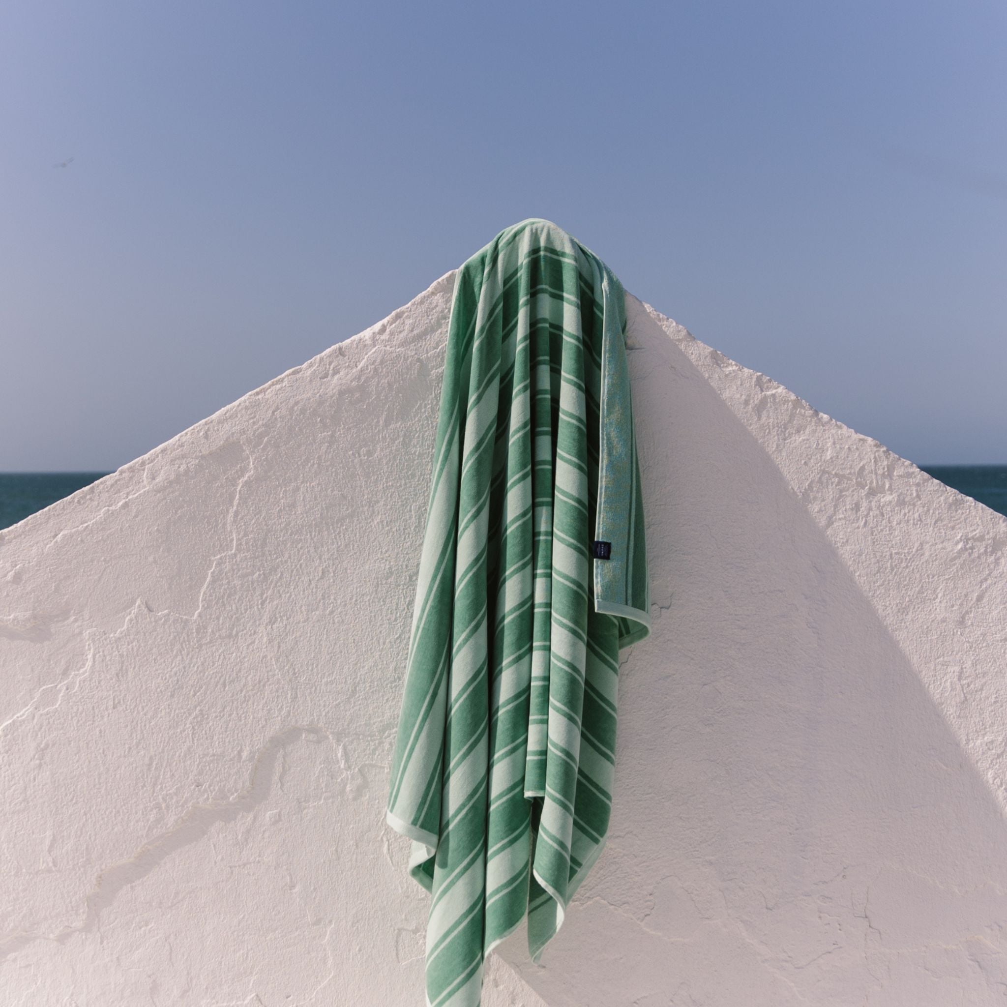 Green striped beach towel draped over a white wall with a blue sky background