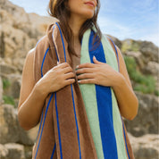 A person holding a striped beach towel with vertical color bands of blue, brown, and green.
