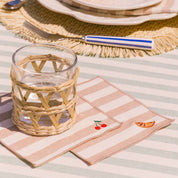 Woven glass on a striped tablecloth with a striped napkin featuring embroidered designs of orange and cherry.