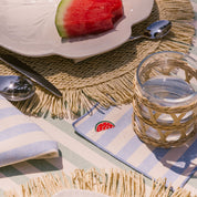 Table setting with watermelon, glass, and striped napkin on a textured tablecloth.