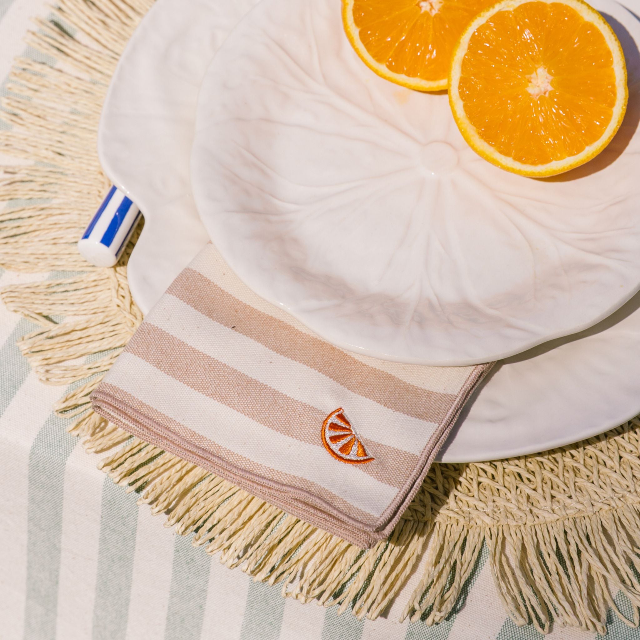 Striped napkin with orange slice design on a woven placemat with sliced oranges