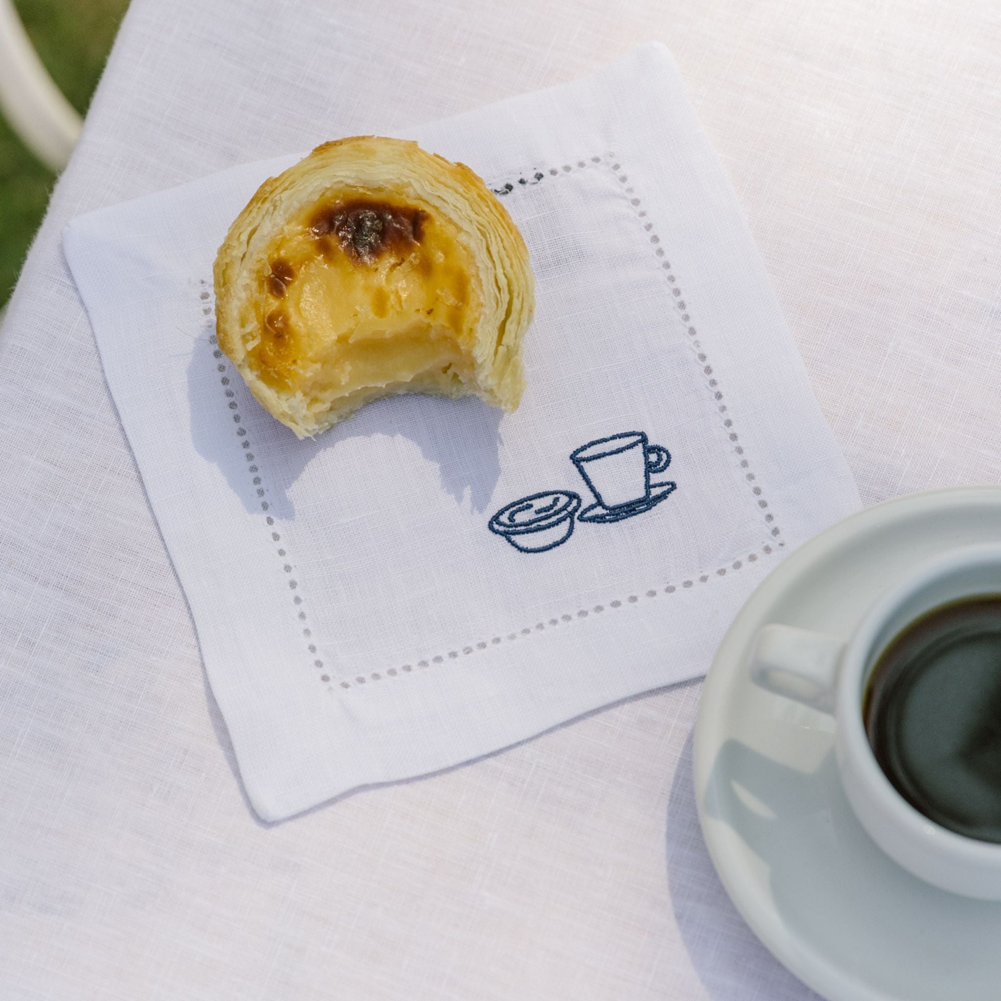 Pastel de nata on a white napkin with a cup of coffee next to it.