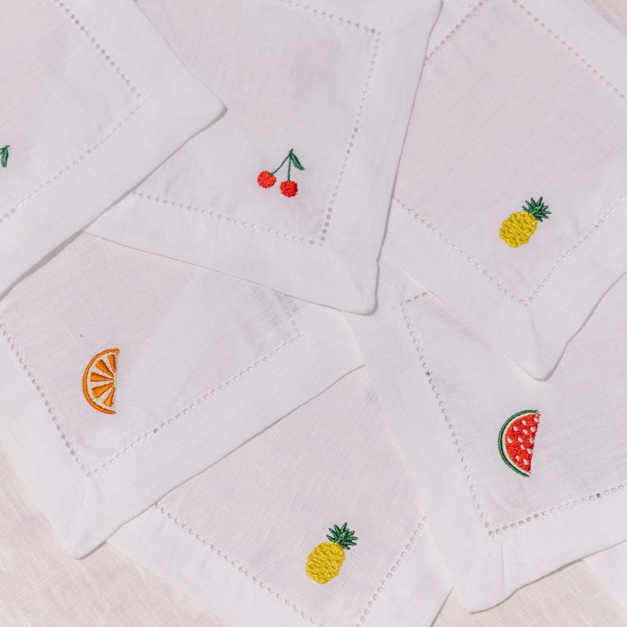 White quilted cocktail napkins with embroidered fruit designs on a beige background